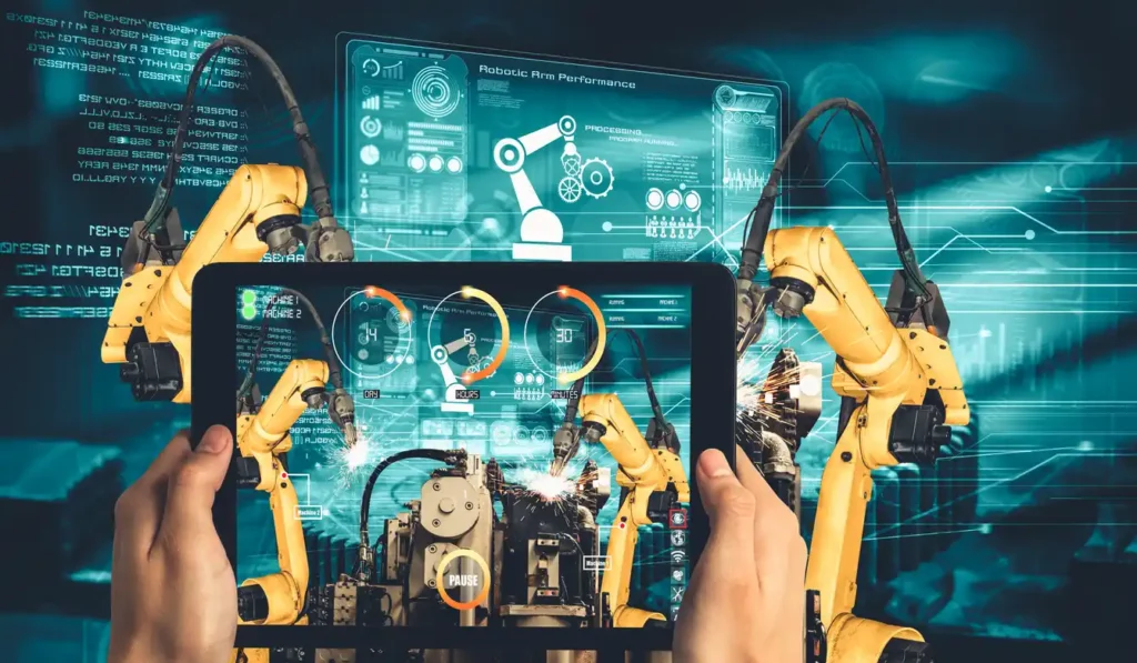 human holding a screen controlling robotic arms in manufacturing