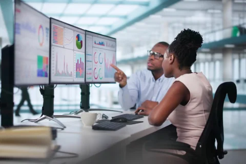 coworkers discussing continuous improvement metrics on computer dashboard