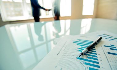 Business documents with charts on the table with business people in the background
