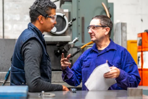 Plant manager reviewing flow and constraints with a supervisor on a manufacturing floor shows operational excellence leadership behavior in practice