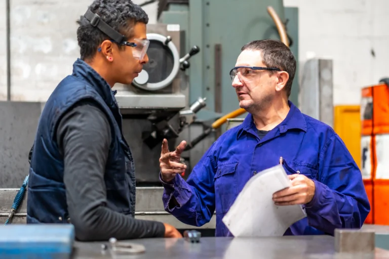 Plant manager reviewing flow and constraints with a supervisor on a manufacturing floor shows operational excellence leadership behavior in practice