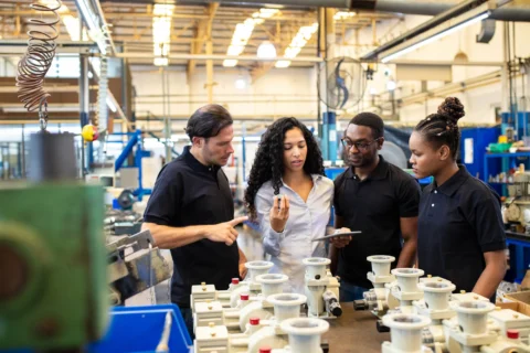 Plant supervisor reviewing staffing levels with operators on a manufacturing production floor, the setting where overstaffing in manufacturing starts.