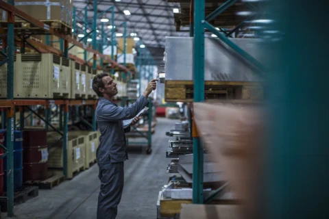 Worker auditing staged work-in-process inventory on warehouse racks — making WIP visible and governed.