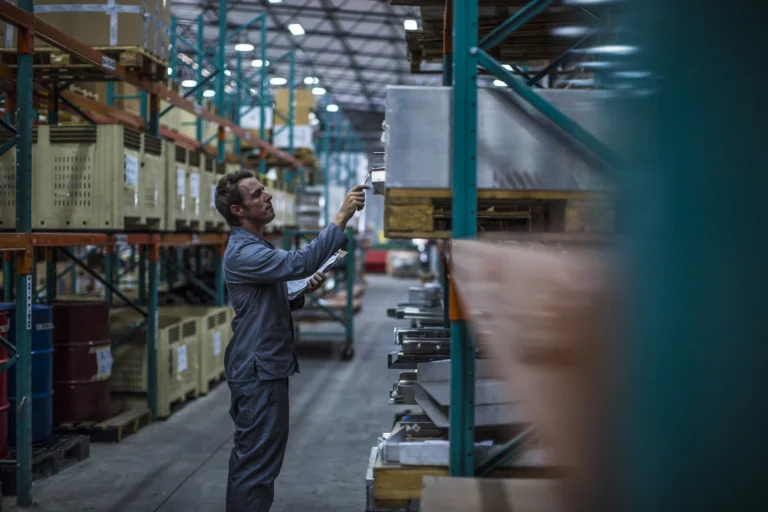 Worker auditing staged work-in-process inventory on warehouse racks — making WIP visible and governed.